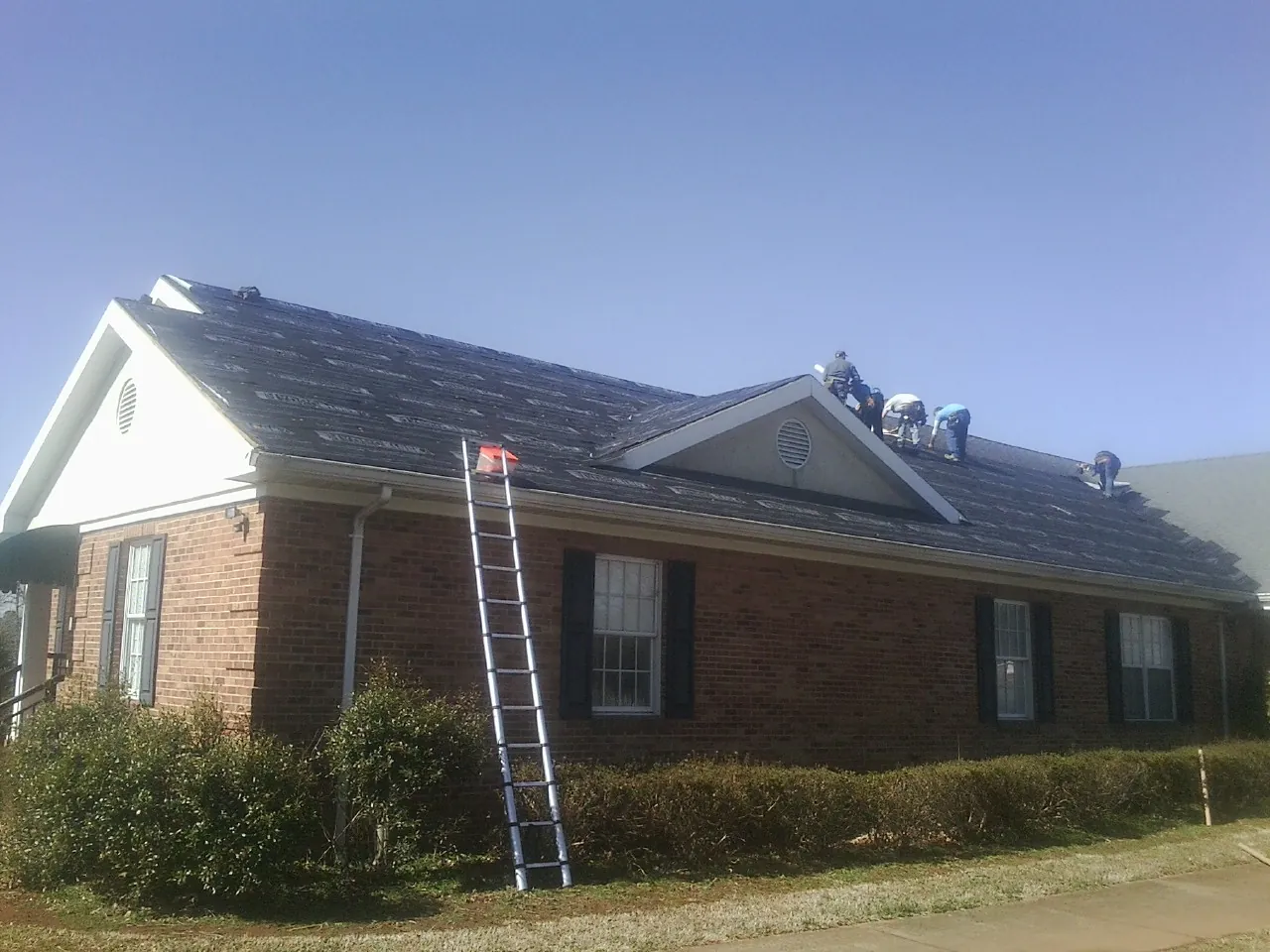 Crew tearing shingles off a brick ranch roof with a ladder set — Emergency Roof Repair work by our crew in La Salle