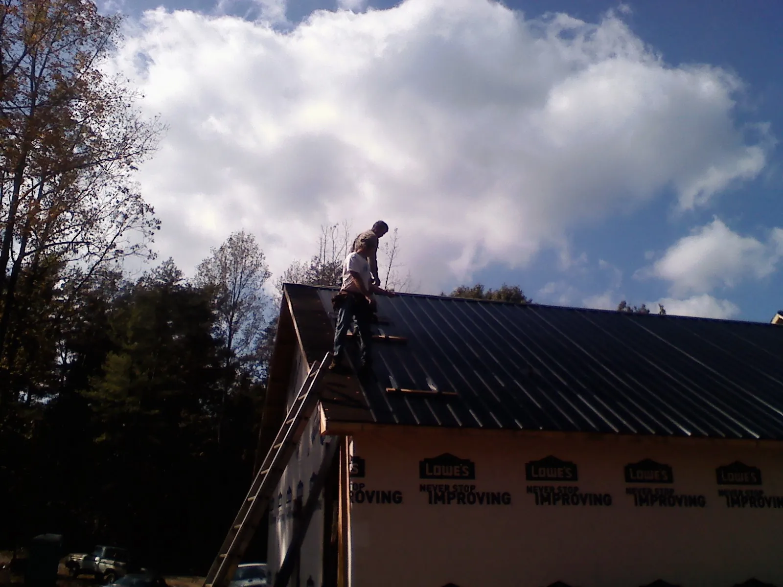Roofer fastening dark metal panels high against a cloudy sky, from a Roof Inspection job in La Salle