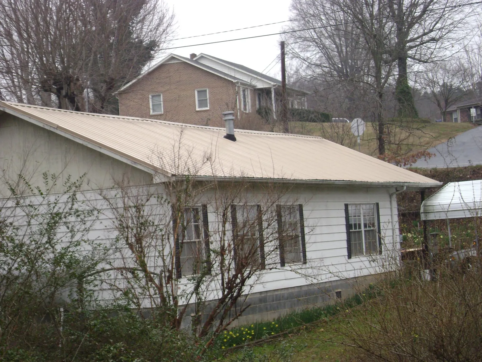 Tan metal roof on a white sided house set into a hillside — Commercial Roofing by Roofing Brothers in La Salle