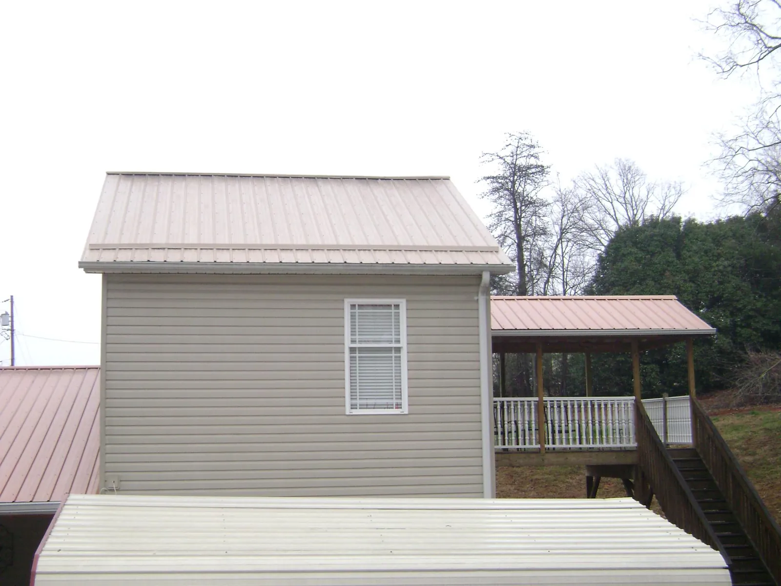 Tan metal roofs on a two story addition and attached porch, from a Roof Replacement job in La Salle